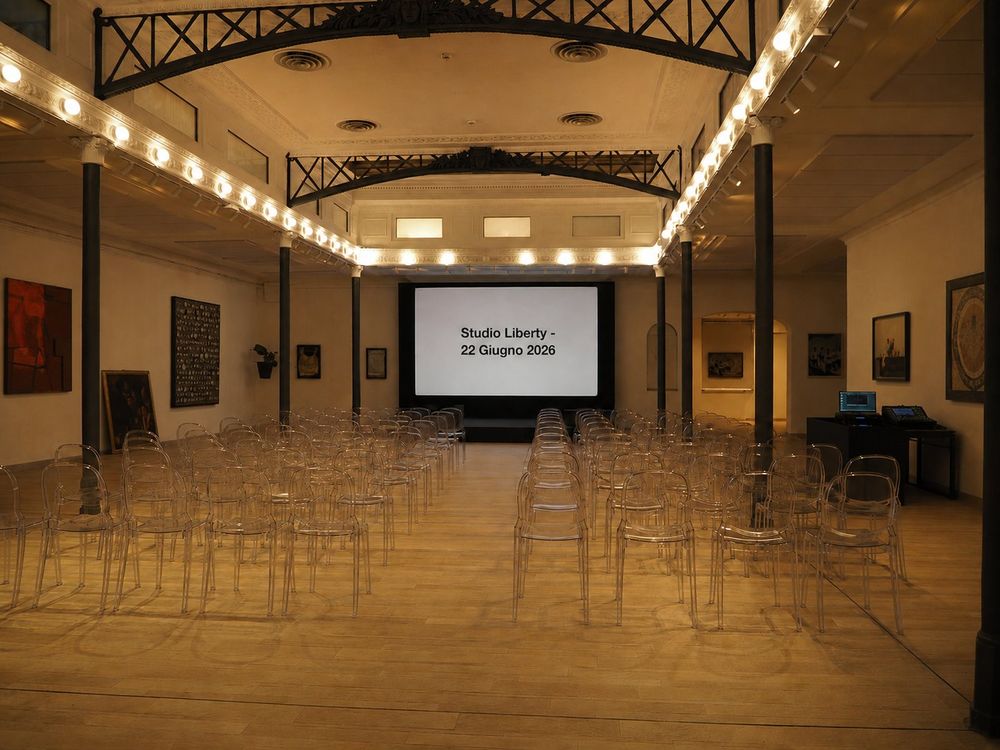 Studio Liberty — assemblea allestita a platea con sedie trasparenti e schermo