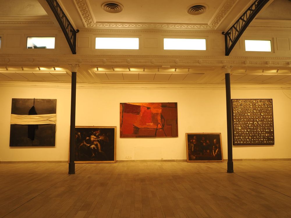 Studio Liberty — parete espositiva con opere contemporanee e dipinti antichi appoggiati a terra